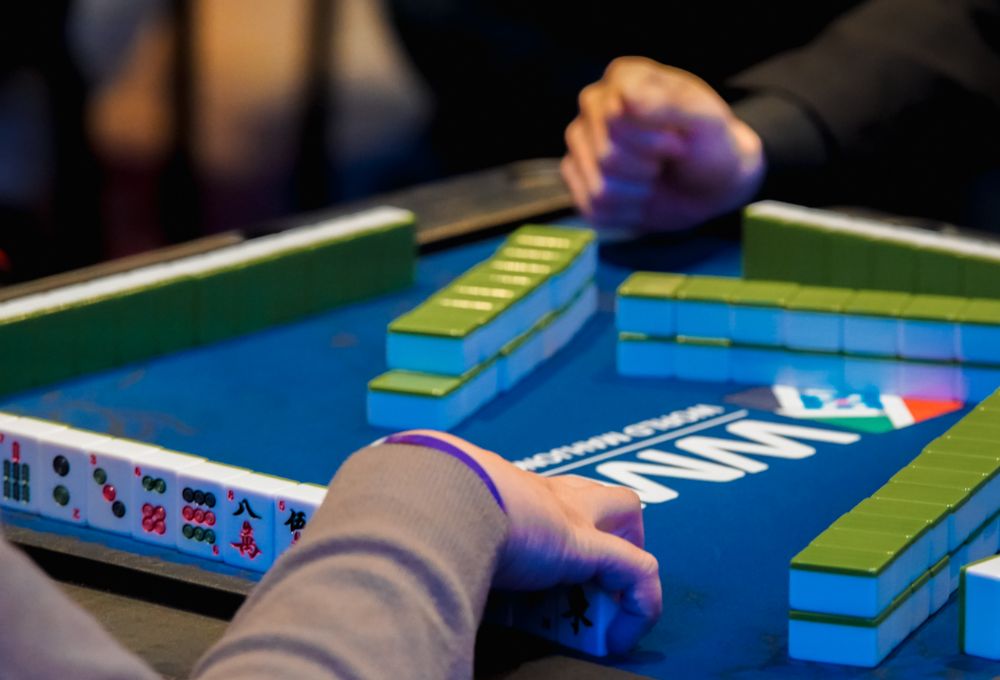 A hand about to place a tile on a mahjong table with stacked tile racks.