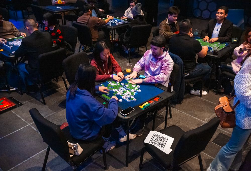 Group of players seated around a poker-style table in a casino-like setting, cards and chips in play.