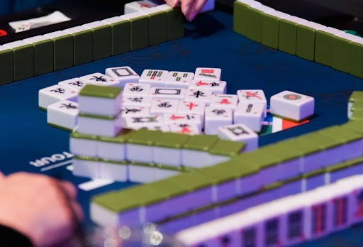Tabletop view of a large pile of Mahjong tiles on a blue felt table, with green tile racks along the border.